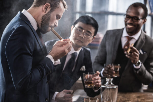 multicultural business team spending time, smoking cigars and drinking whiskey